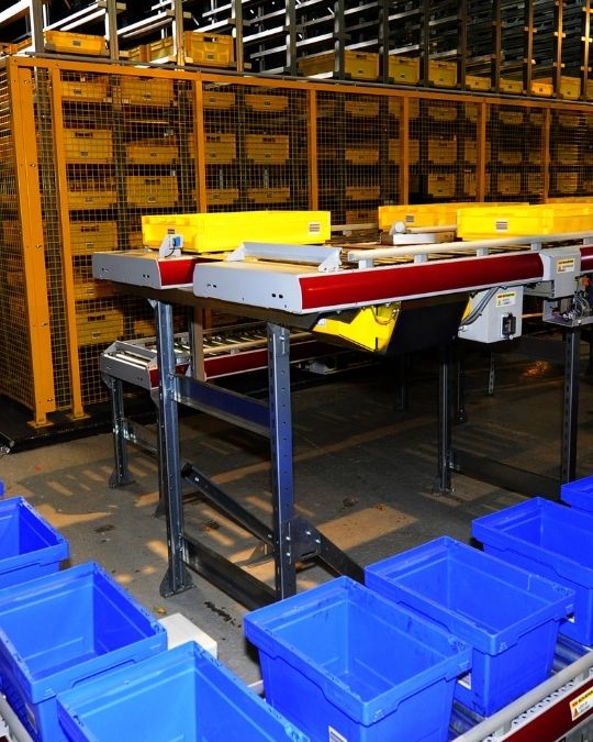 Zone de picking en entrepôt logistique avec bacs de prélèvement et convoyeur automatisé