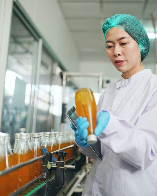 Technicienne en tenue de protection contrôlant des bouteilles sur une ligne de production agroalimentaire